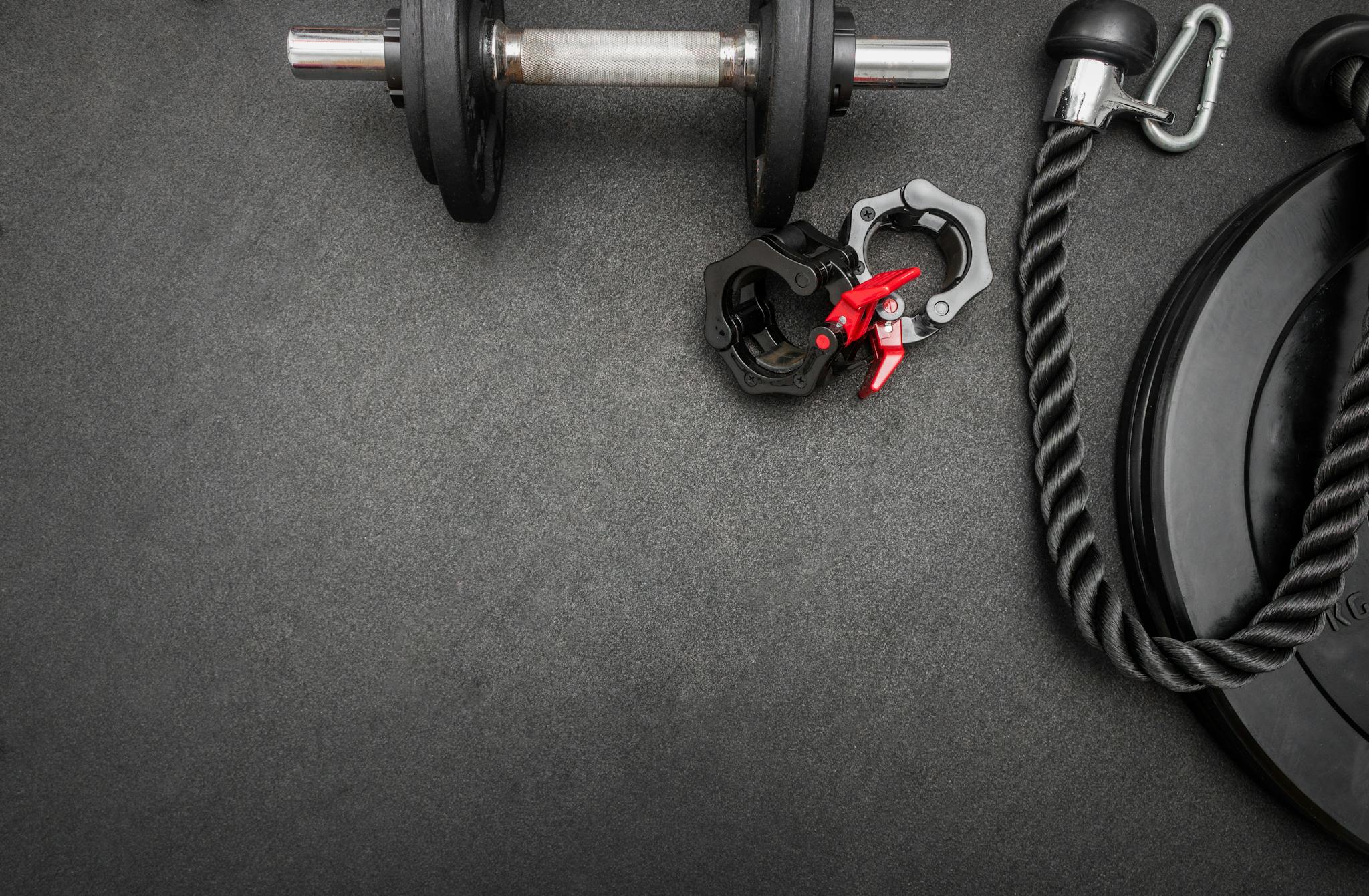 Barbell, dumbbells, triceps rope and clamps on the floor at the gym. Top down view flat lay with bodybuilding equipment on a black background and empty space for text. Fitness, weight trai...